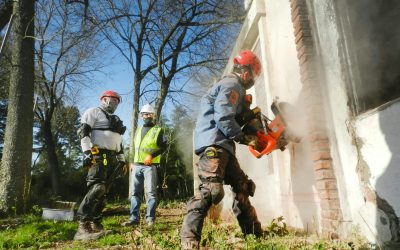 pexels-photo-8215884-8215884-1 Construction workers dressed in safety gear demolishing a brick wall with heavy machinery outdoors.